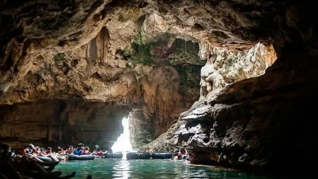 Wisatawan berperahu di sungai bawah tanah gua kapur, diterangi cahaya alami dari celah atas di Goa Pindul Jogja.