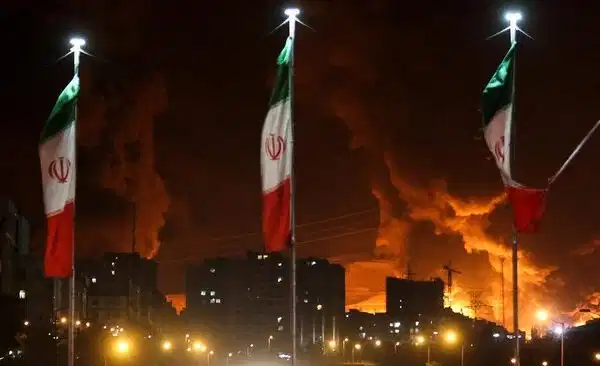 bendera iran berkibar saat api dan asap dari serangan israel terhadap depot minyak sharan membubung menyusul serangan israel t 1749980176957 169